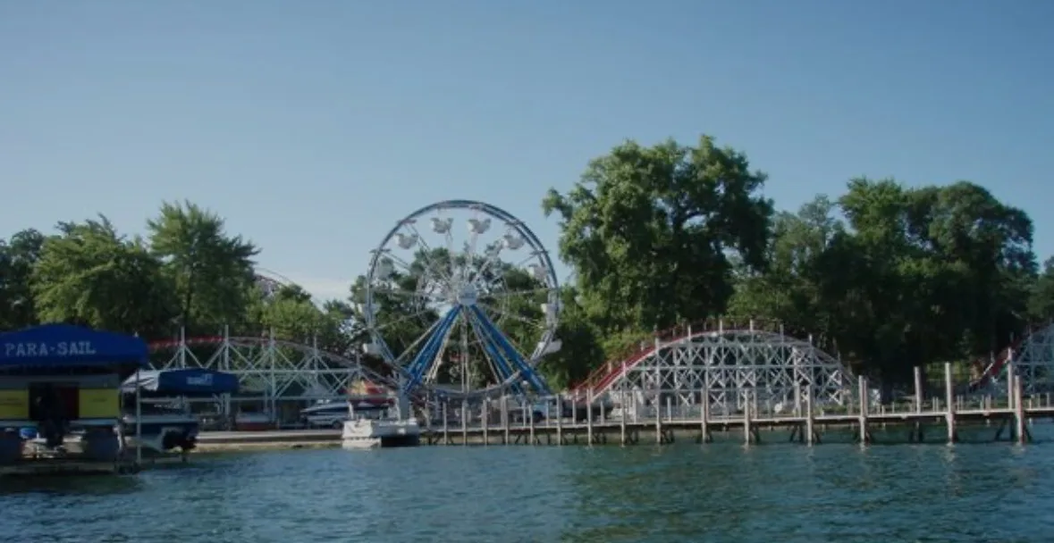 A roller coaster and Ferris wheel rise behind the waterfront at Arnolds Park.