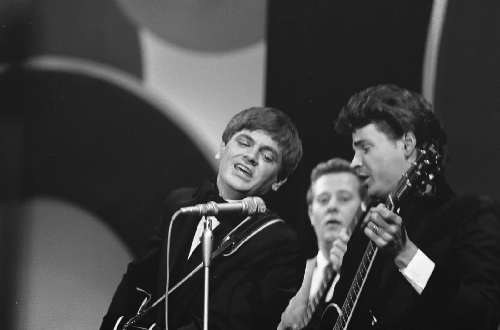 Black-and-white archival photograph of the Everly Brothers singing into a shared microphone while playing guitars.