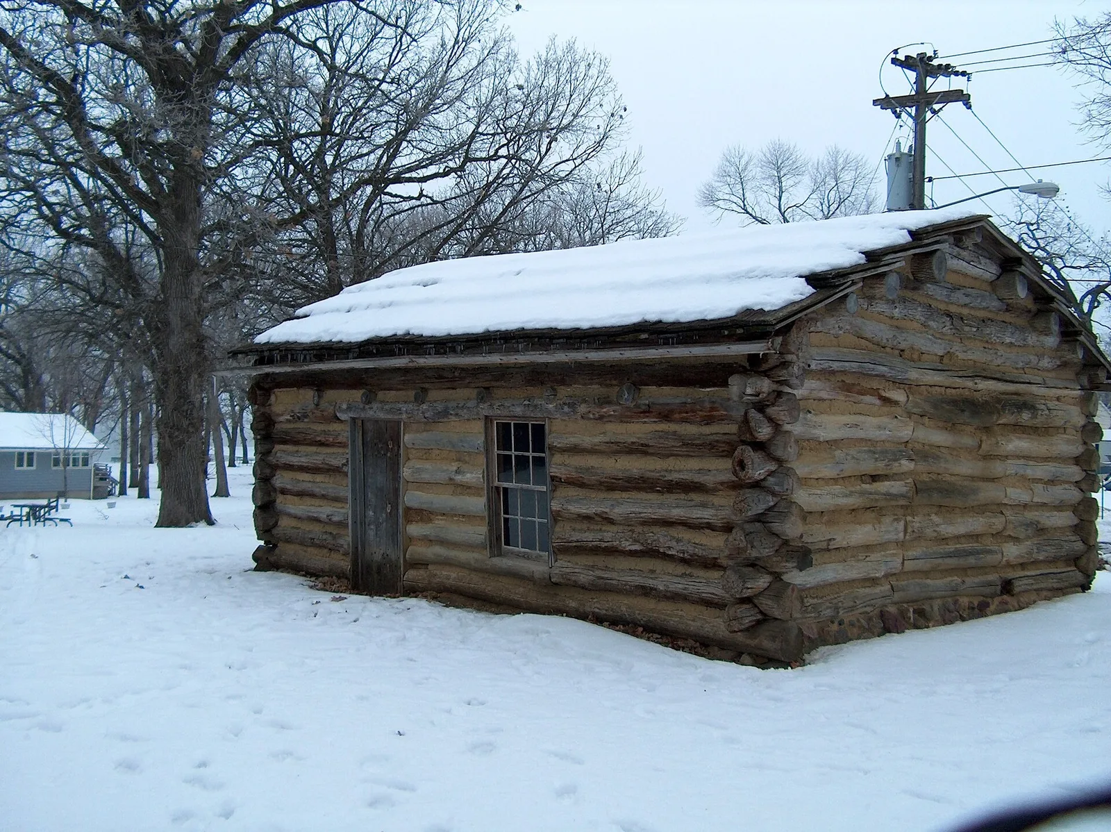 A small log cabin stands among bare trees and snow.